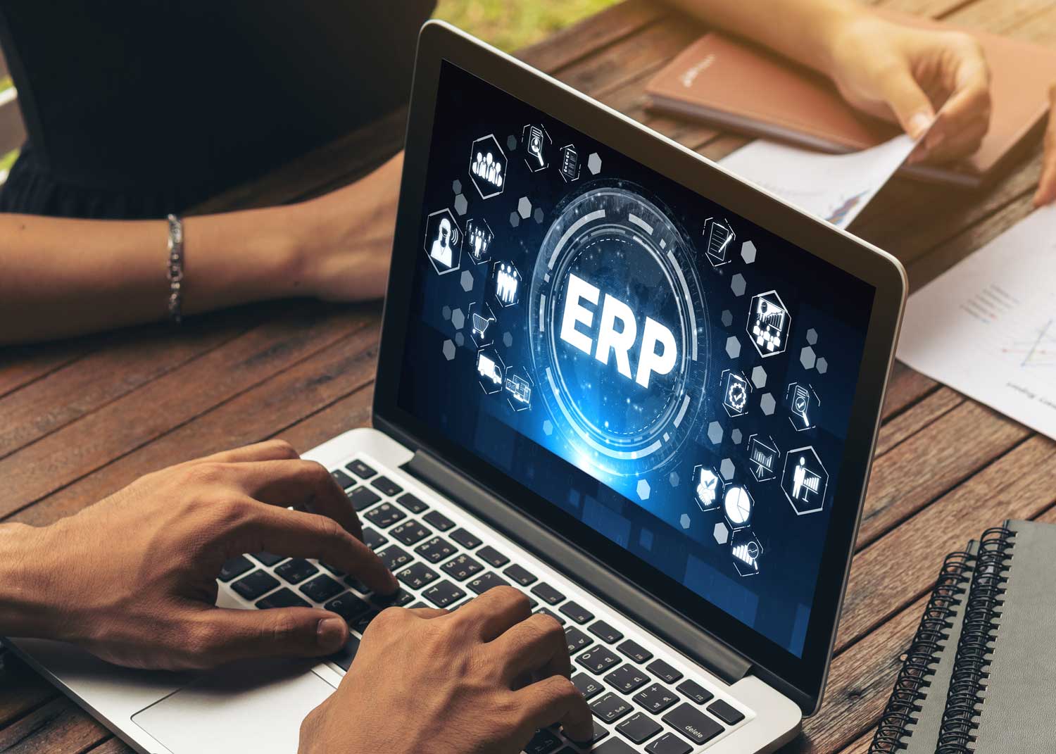 A man works at a laptop at a tale shared with other office workers. On the laptop screen are the letters ERP