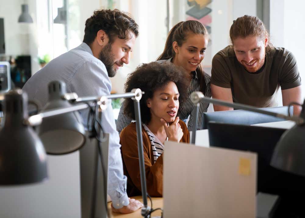 A team of salespeople huddles behind a computer discussing work